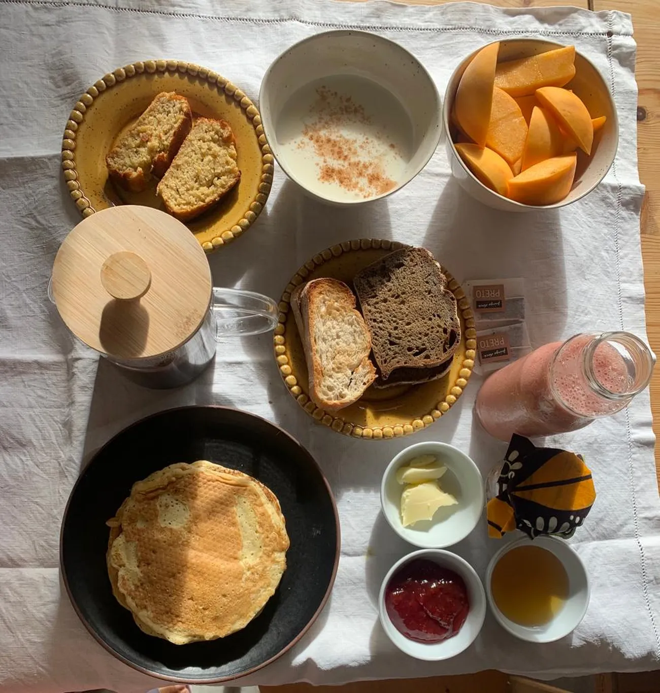 Mesa de pequeno-almoço completa, com panquecas, pão, fruta e sumo